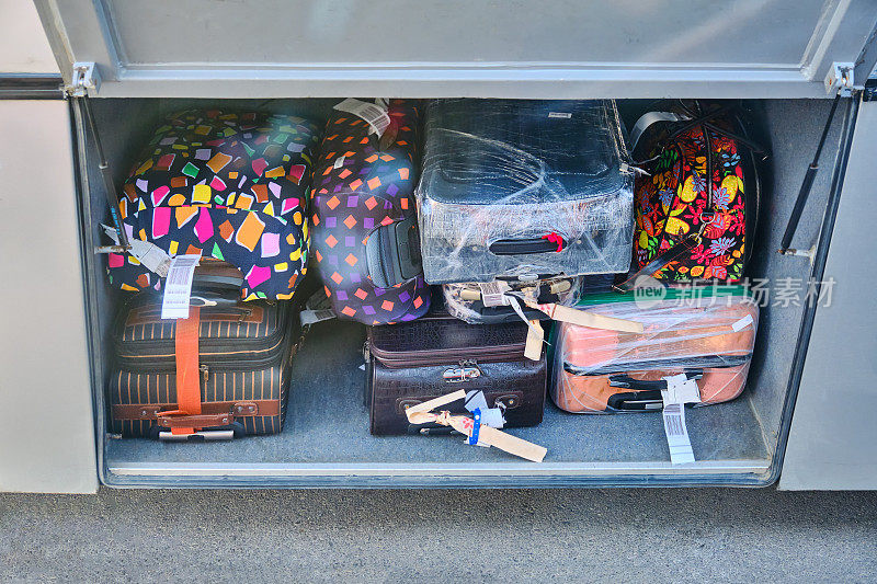 在公共汽车上托运行李或手提箱。许多沉重的行李被装入公共汽车的储物柜。旅行时打包行李。公共汽车行李厢里的行李箱。