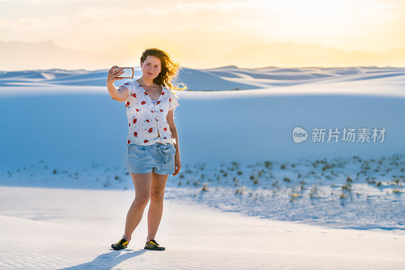 一名女子在新墨西哥州白沙沙丘国家纪念碑的沙丘上用手机自拍