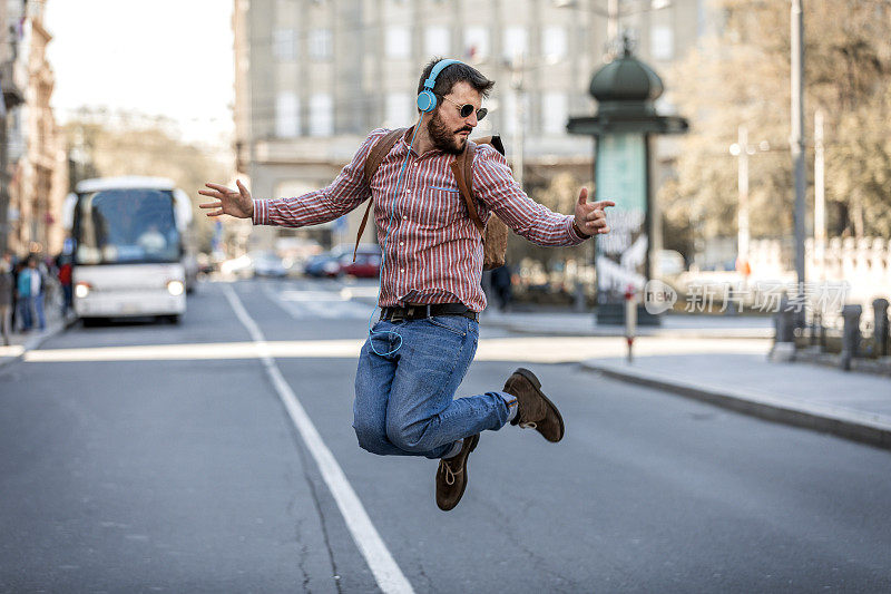 一个年轻人在城市的路上跳舞。快乐的人一边听音乐一边悠闲地跳舞。