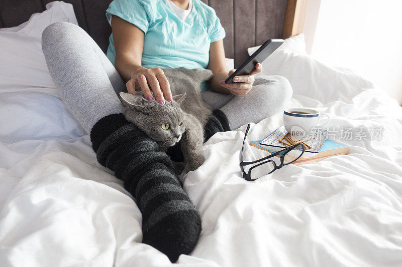 家里的床上有猫、咖啡和智能手机的女人