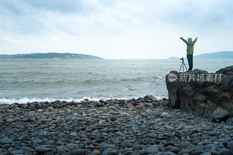 一位男艺术家在海边的悬崖上拍照。