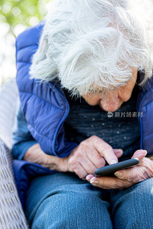 年长的白人妇女密切关注和使用智能手机的触摸屏在户外