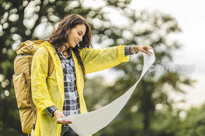 年轻女子穿着防水夹克，看地图，在雨中徒步旅行