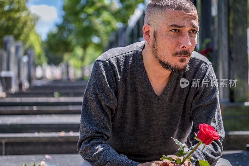 一个人在墓地的坟墓上放了一朵红玫瑰。在失去所爱之人后的基督教传统