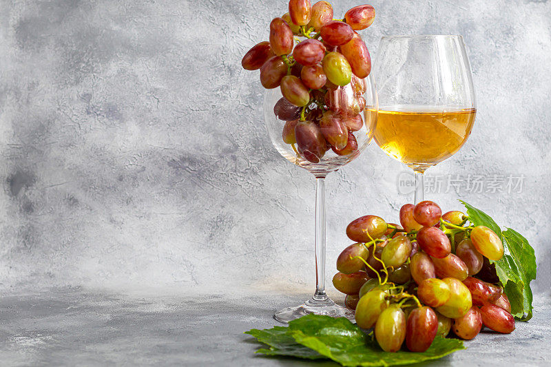 大而淡的葡萄酒葡萄。它被一层白色的酵母覆盖。杯子里盛的是淡葡萄酒。水滴在浆果上。在一个灰色的背景。