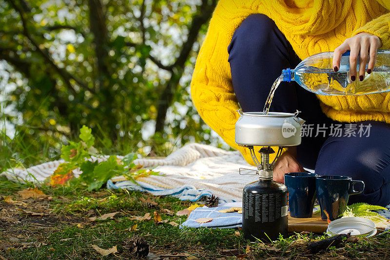穿着黄色毛衣的年轻美丽的女孩在森林里用煤气炉煮咖啡。在秋天的森林里，用primus的火炉一步一步地煮咖啡
