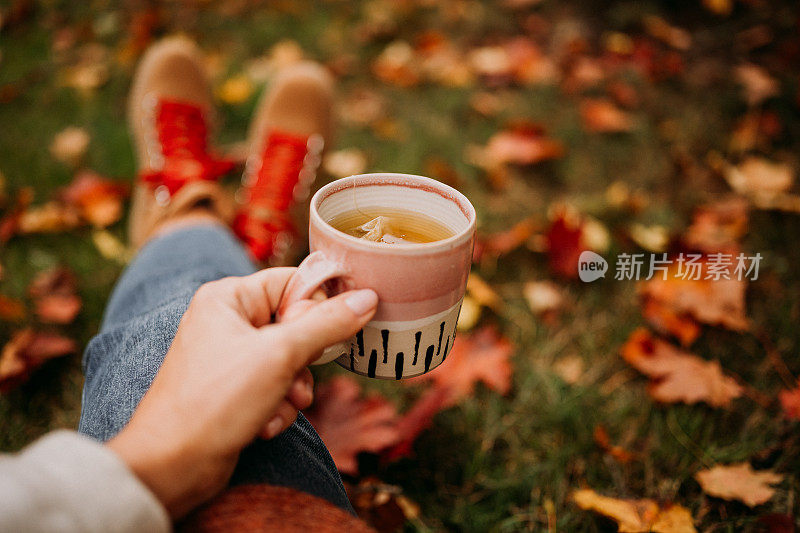 在户外喝茶的女人在秋天休闲装近陶瓷茶杯