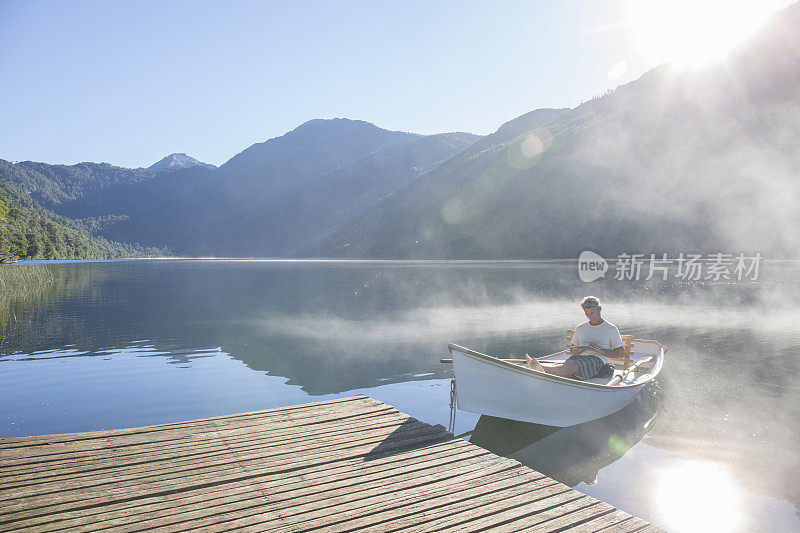 一名男子在宁静的湖面上划着小船休息