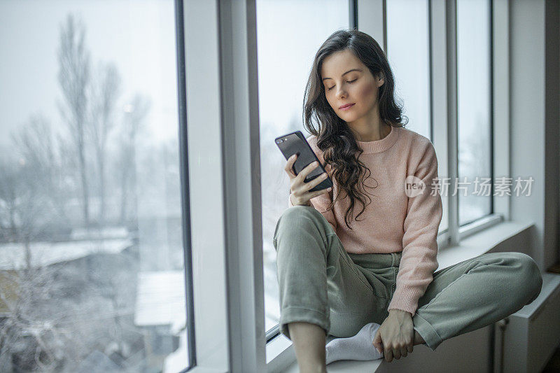 抑郁的女人在家里感到难过。女人悲伤地看着窗外。一个沮丧孤独的女人独自站在那里，一边打电话一边看窗外。