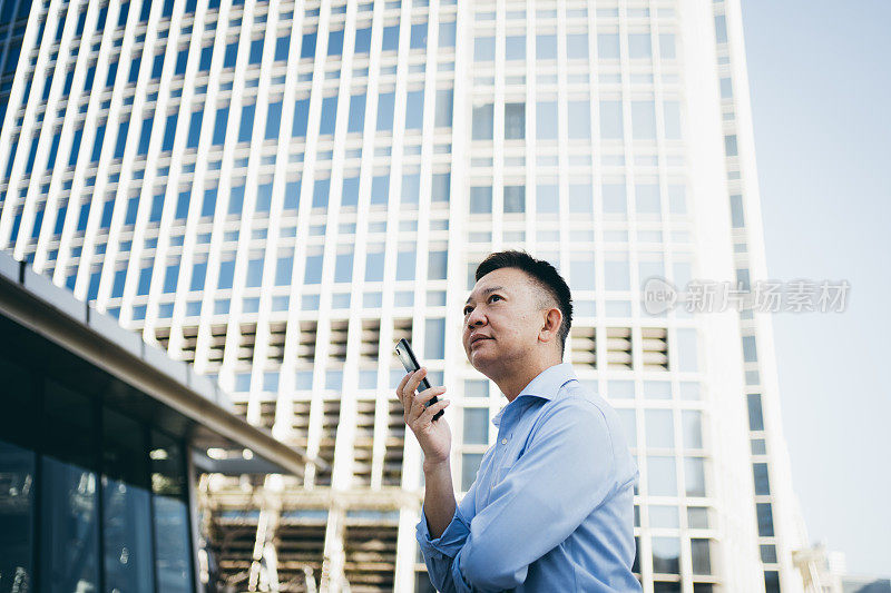在香港的金融区，亚洲资深商人拿着智能手机仰望天空