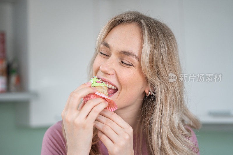 年轻女子微笑着，在厨房里咬着纸杯蛋糕