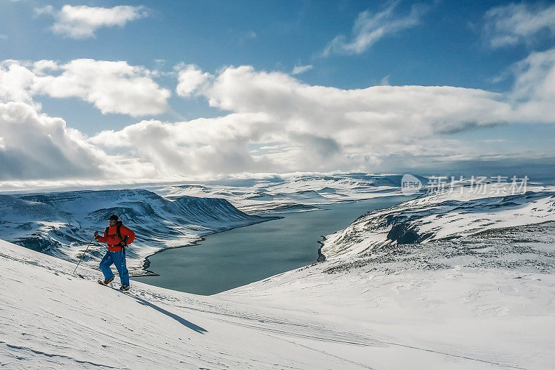 (全景)一名高大的登山者身穿红色夹克，手持登山杖，登上冰岛霍恩斯特兰迪尔雪山的山顶