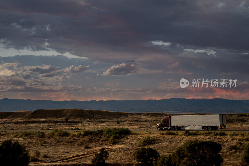 黄昏时分，在戏剧化的天空下，半卡车在犹他州沙漠的高速公路上超速行驶