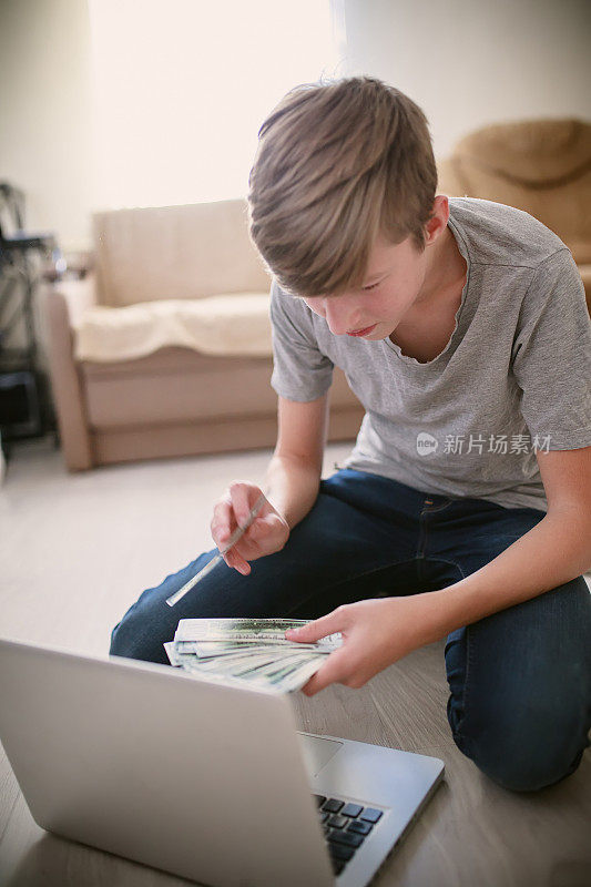 十几岁的自由职业者在笔记本电脑上计算着网上挣来的钱，对收入很满意。男孩在网上学习，在家舒舒服服地赚钱。孩子在电话会议上数钱给朋友看。