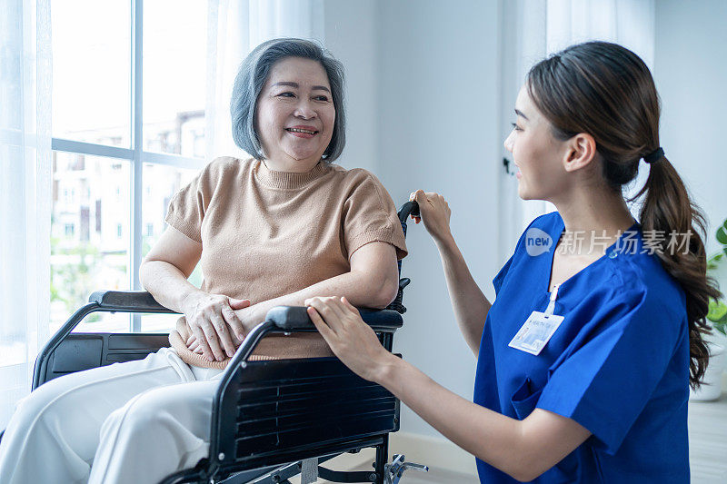 亚洲护士照顾老年妇女轮椅在护理之家。迷人快乐的看护者女孩医生照顾老年老年残疾患者女性到医院病房的窗口看瓯