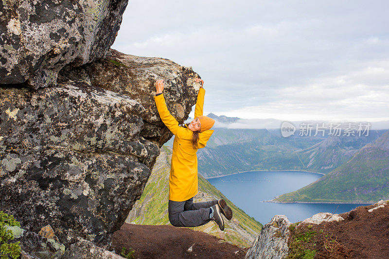 身着黄色雨衣的妇女，被吊在挪威北部Senja岛的Segla山的岩石上。令人惊叹的美丽风景和壮丽的自然