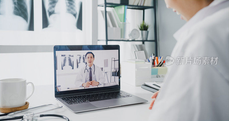 身穿白色医疗制服的年轻亚洲女医生使用笔记本电脑与在健康诊所或医院的办公桌上的高级医生进行视频会议。