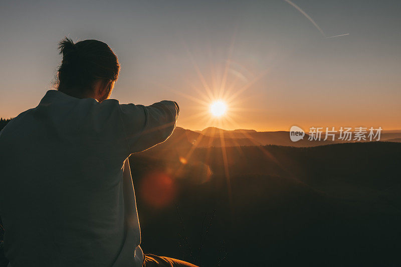 一个年轻人在日落时分从山顶上指着太阳