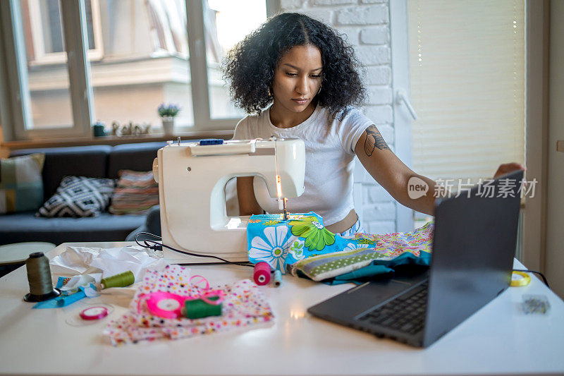 年轻的女裁缝和女商人使用笔记本电脑和缝纫机