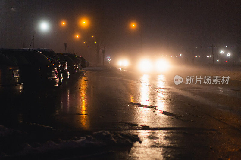 多雾的天气。夜雾。路面能见度低。汽车的运动。交通堵塞。湿滑的沥青。汽车头灯。一缕光。路上有冰雪。城市街道