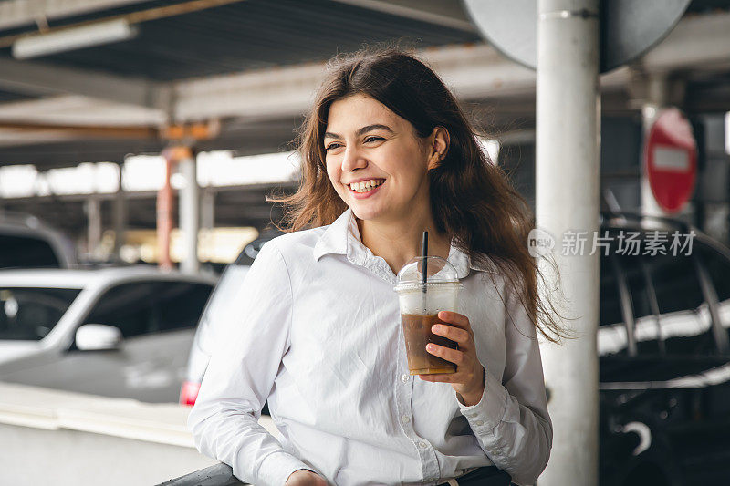 有魅力的年轻女商人在停车场喝着咖啡。