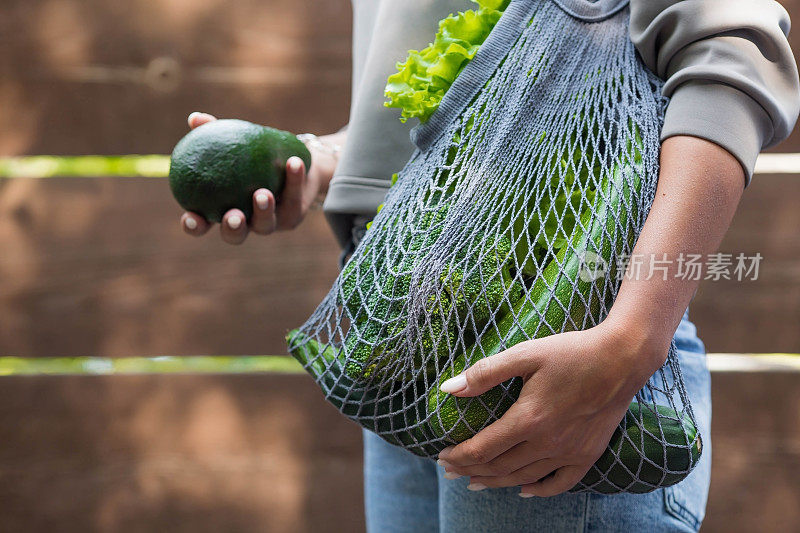 女性用手串线包和青菜特写。一个买食物的女孩。健康营养、素食和生态的概念。拒绝使用塑料袋。