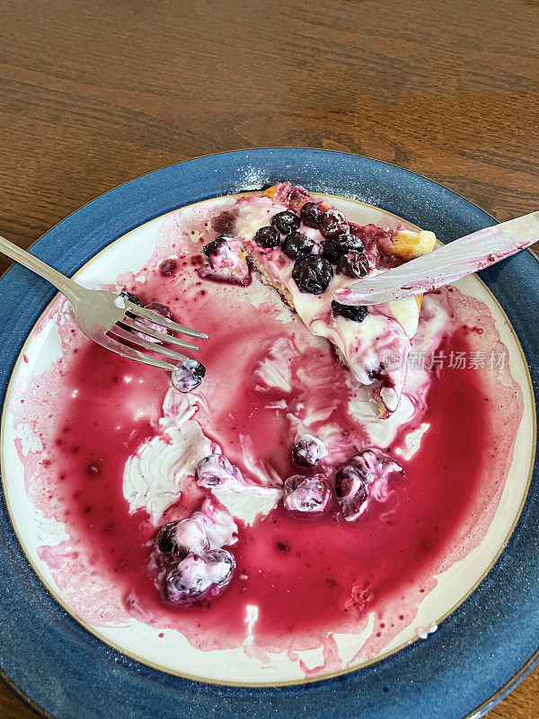 吃了一半的早餐的图像自制的比利时华夫饼，上面有天然酸奶，樱桃和蓝莓，撒上糖霜，桌子上有蓝色边框的盘子，叉子，刀，高架视图，重点在前景
