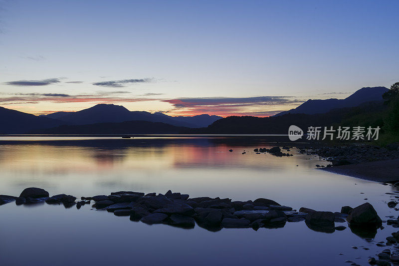 在英国苏格兰特罗萨克斯的洛蒙德湖平静的水面上看日落