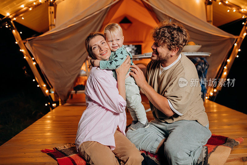 幸福的家庭和可爱的宝宝一起放松，在夏天的晚上一起在舒适的篝火旁露营。户外休闲休闲的豪华露营帐篷。生活方式的概念