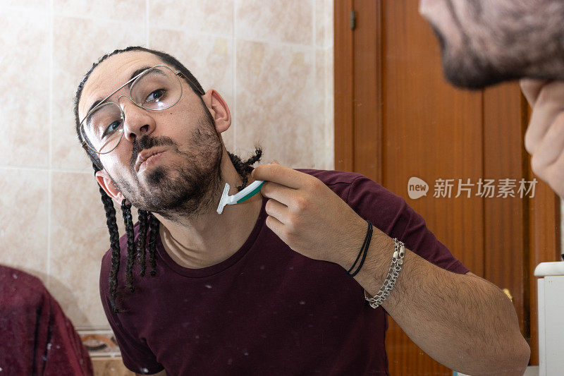 一个男人在镜子前用剃刀刮胡子。镜子里年轻男子剃须的倒影。成年男子用剃刀刮胡子
