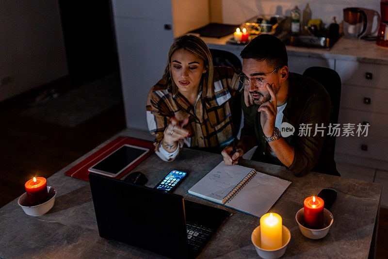 在一次精力充沛的危机中，一对年轻夫妇在黑暗中点着蜡烛，用笔记本电脑工作。