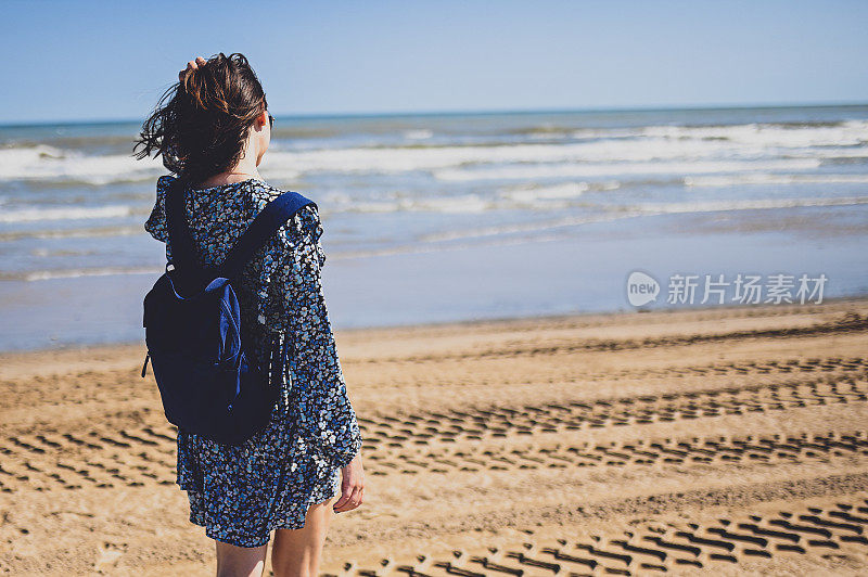 中年成年妇女走在海边的背景。清新的海风吹拂着她的头发