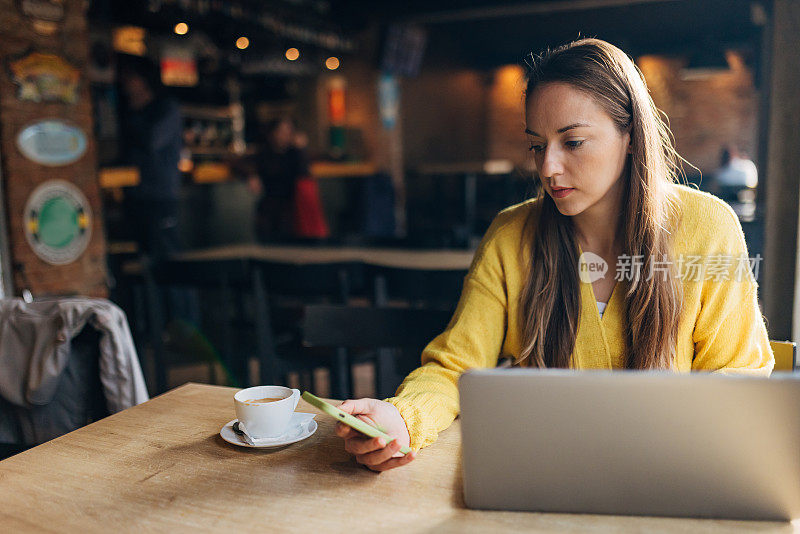 商业女性在咖啡店喝咖啡，使用智能手机和笔记本电脑