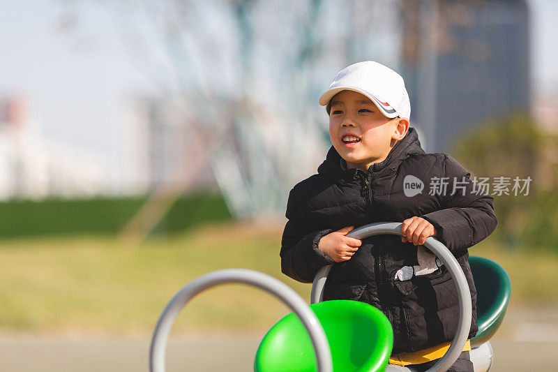 可爱的亚洲男孩在户外操场上玩跷跷板。