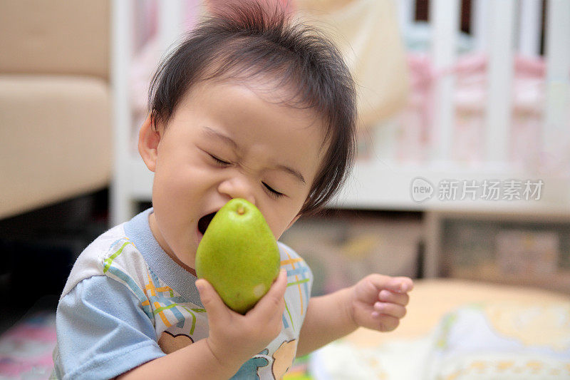 一个亚洲婴儿正试图咬一个水果