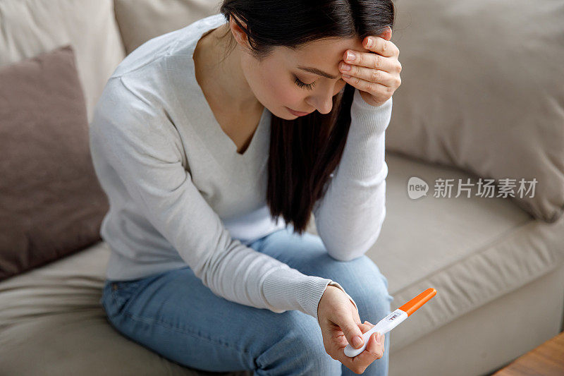 一个悲伤的女人手里拿着验孕棒。意外怀孕的概念。