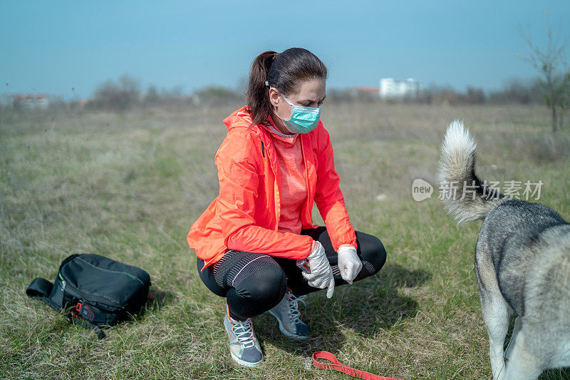 戴着防护口罩的年轻美女和她的白狗在公园外面的草地上休息