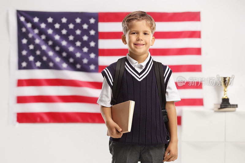 穿着制服的男生拿着一本书，在美国国旗前微笑