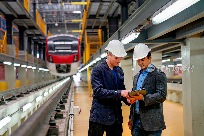 职业经理或工程工人在工厂的电气或地铁列车前与平板电脑一起讨论。