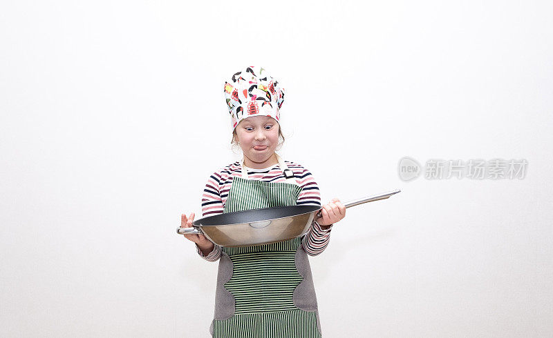 一个8岁的白人小女孩，一个小厨师，手里拿着一个大煎锅，开心地笑着。在浅色背景上的肖像。