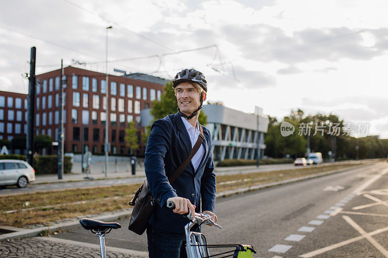 英俊的中年男子骑着自行车穿梭于城市之间，在自行车旁边步行过马路。在漫长的工作日后骑自行车下班的男性城市通勤者。