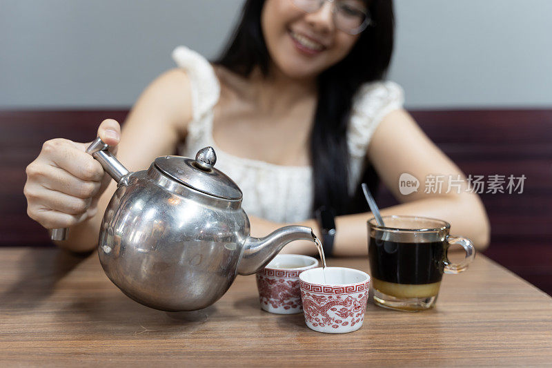 一位妇女正在把茶倒进两个杯子里。