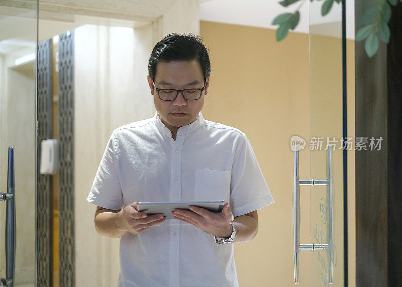 戴眼镜的亚洲商人在晚上使用数码平板电脑
