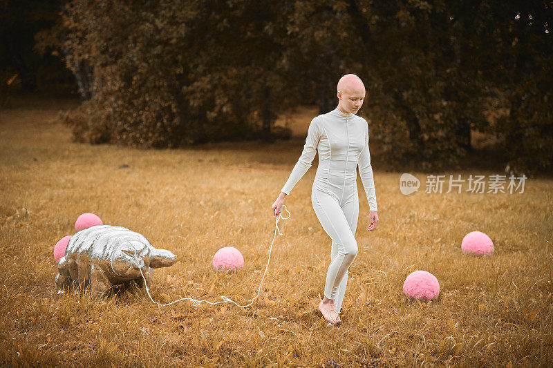在秋天的公园里，穿着白布的秃头小女孩走着缓步动物玩具的肖像
