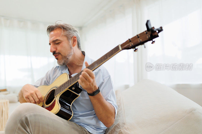 一个成熟的男人在沙发上舒舒服服地弹着原声吉他，在客厅里感受音乐。