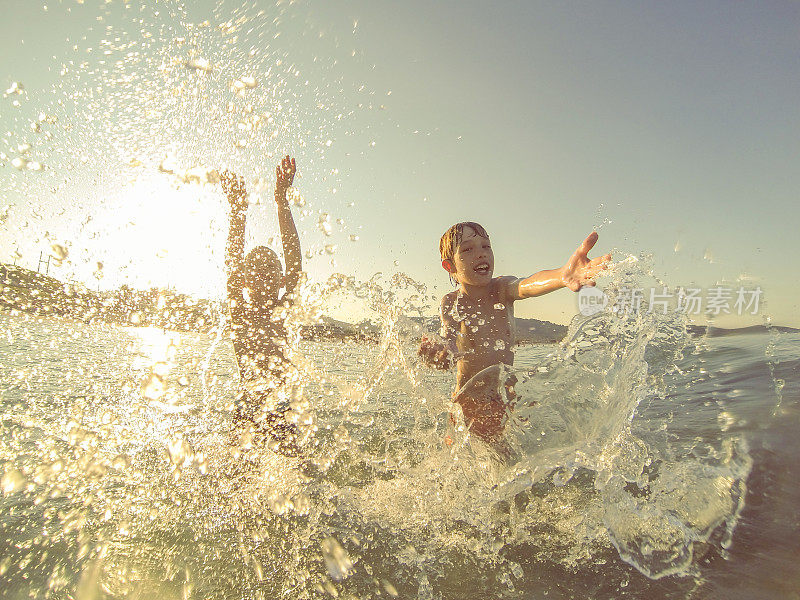 日落时分，男孩们在海里嬉戏，溅起水花