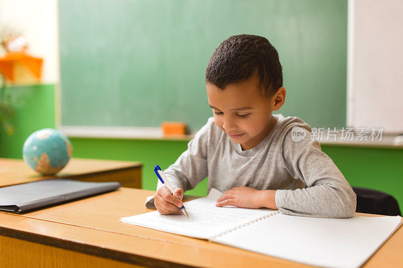 微笑的非裔美国学生在老师的书桌上写笔记本。