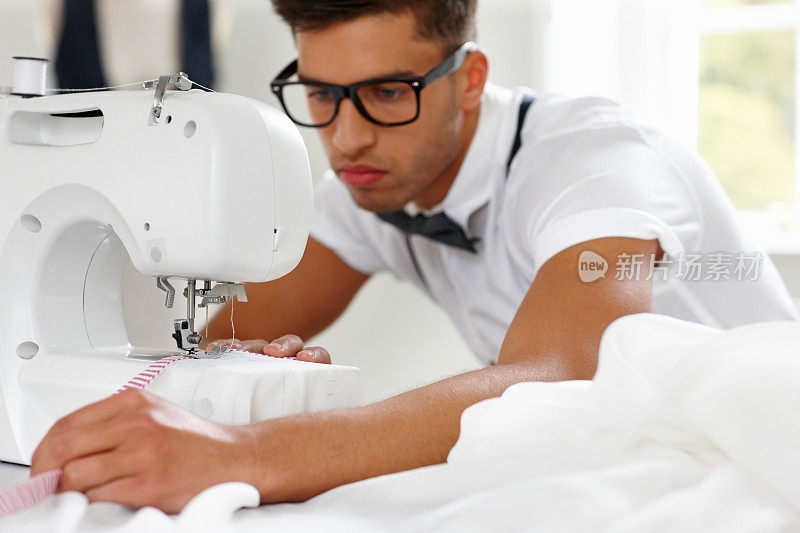 英俊的年轻男裁缝在缝纫机上工作