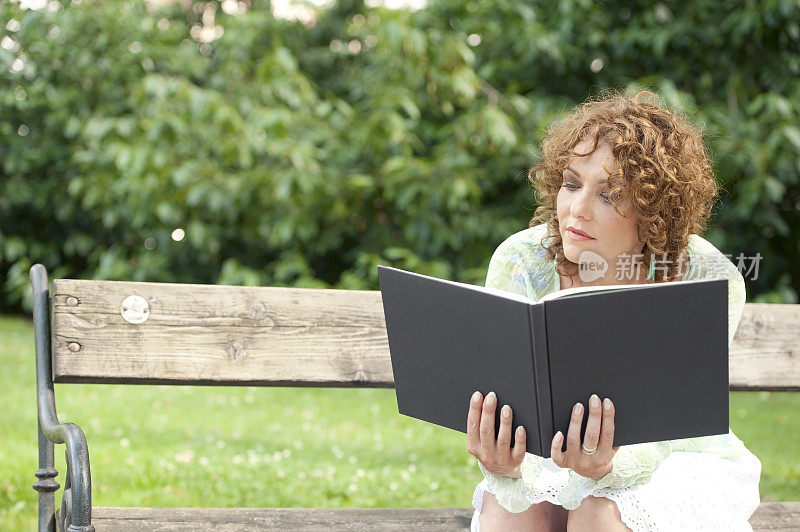 迷人的成熟女人在城市公园里看书