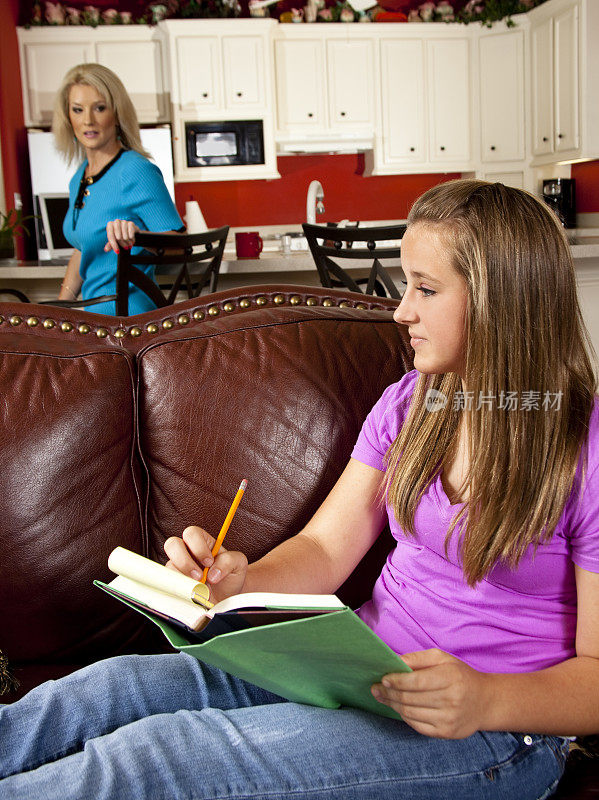十几岁的孩子在沙发上做她的家庭作业，妈妈在厨房工作
